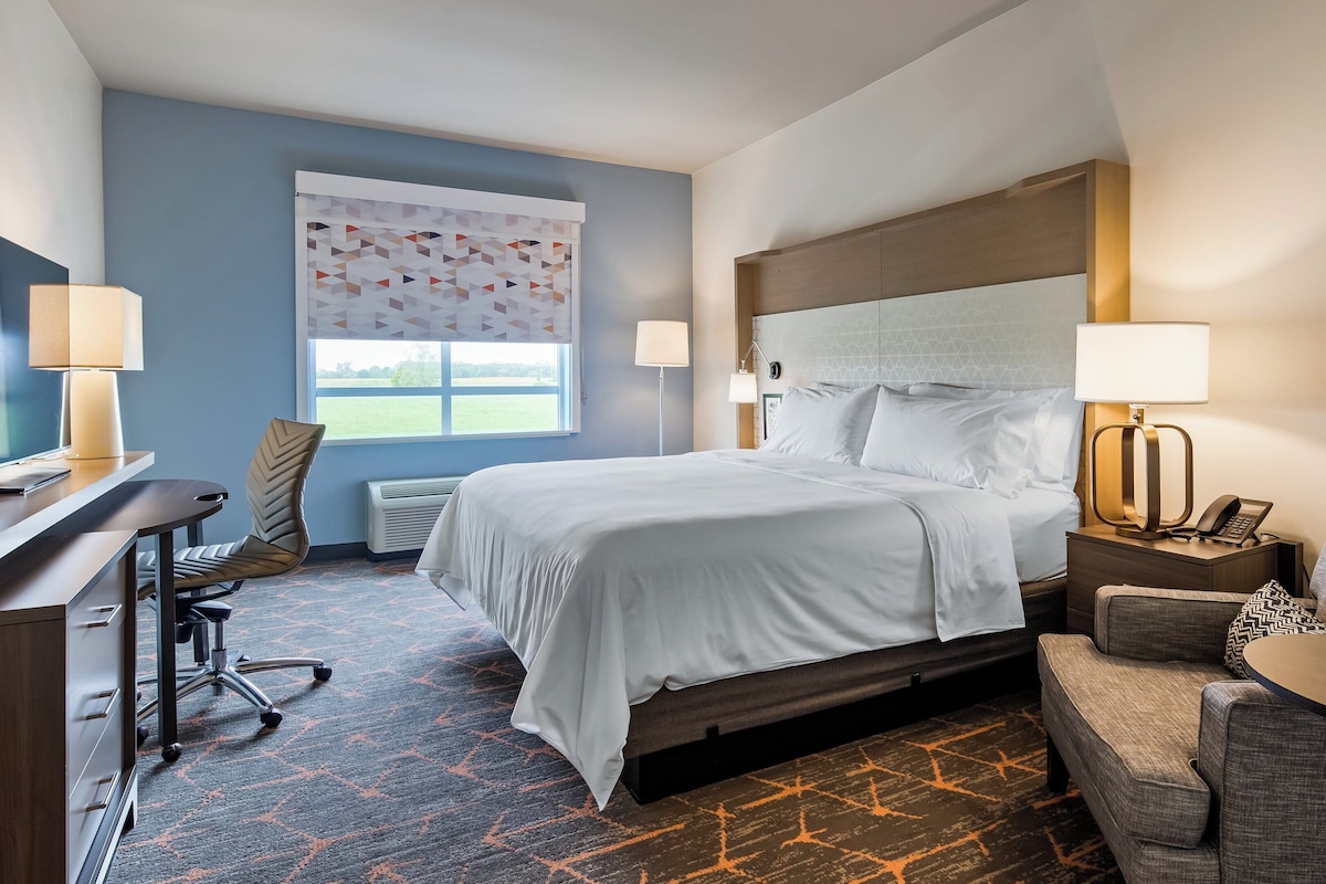 Quarto de hotel com cama, escrivaninha, poltrona, sofá e janela com vista para o exterior.