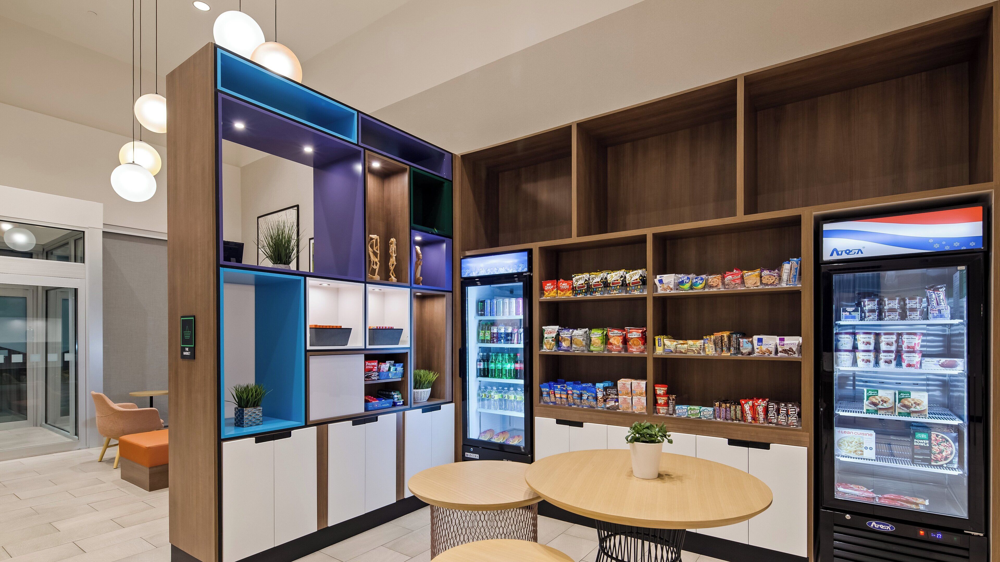 Una kitchenette moderna con electrodomésticos integrados, un refrigerador lleno de aperitivos y una zona de estar con dos mesas redondas.