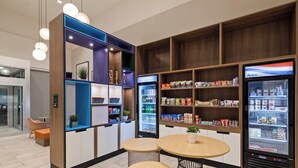 A modern kitchenette with built-in appliances, a refrigerator stocked with snacks, and a seating area with two round tables. - Holiday Inn Clarksville Northeast by IHG (Clarksville)