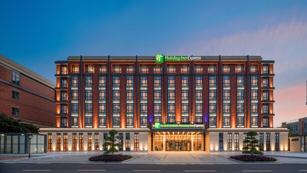 A Holiday Inn Express hotel with a modern facade, large windows, and a well-lit entrance. - Holiday Inn Express Yixing (Wuxi)