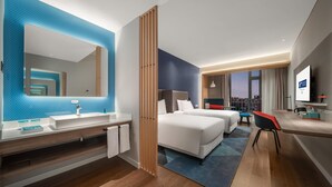 A modern hotel room with a large mirror, a sink, two beds, a desk, and a view of the city. - Holiday Inn Express Yixing (Wuxi)