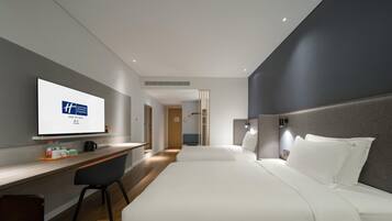 Een moderne hotelkamer met een bed, een bureau en een televisie waarop het logo van het hotel te zien is.