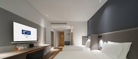 Une chambre d’hôtel moderne équipée d’un lit, d’un bureau et d’un téléviseur affichant le logo de l’hôtel.