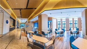 A modern hotel lobby with a central reception desk, seating areas, and a view of the dining area. - Holiday Inn Express Yixing (Wuxi)