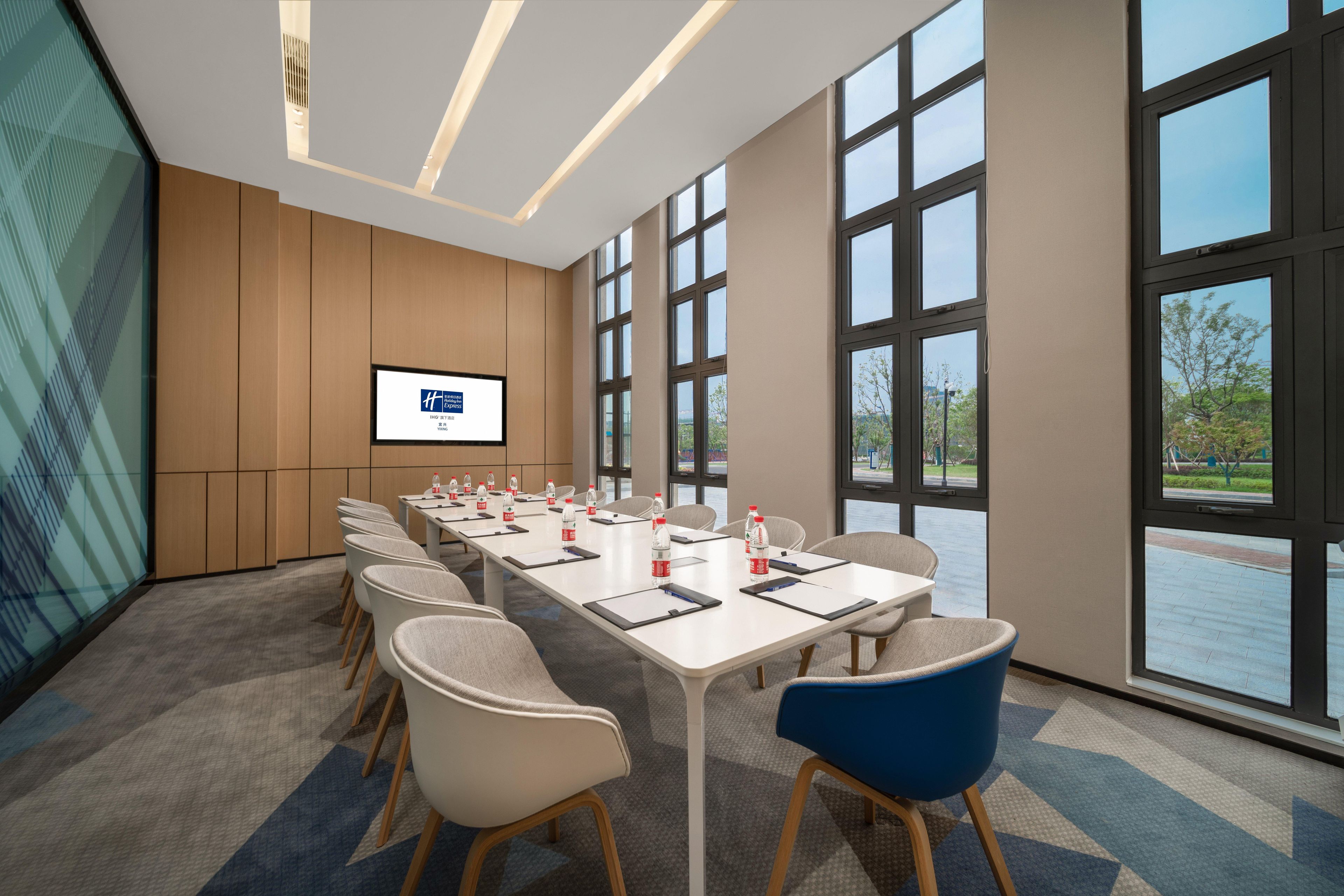 Une salle de conférence avec une longue table, des chaises, un écran et de grandes fenêtres.