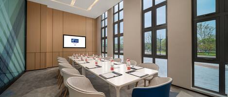 A conference room with a long table, chairs, a screen, and large windows.