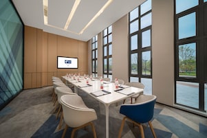 Un salón de conferencias con una larga mesa, sillas, una pantalla y ventanas amplias.