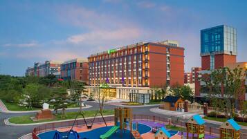 A hotel with a playground, a road, and a building with a green sign.