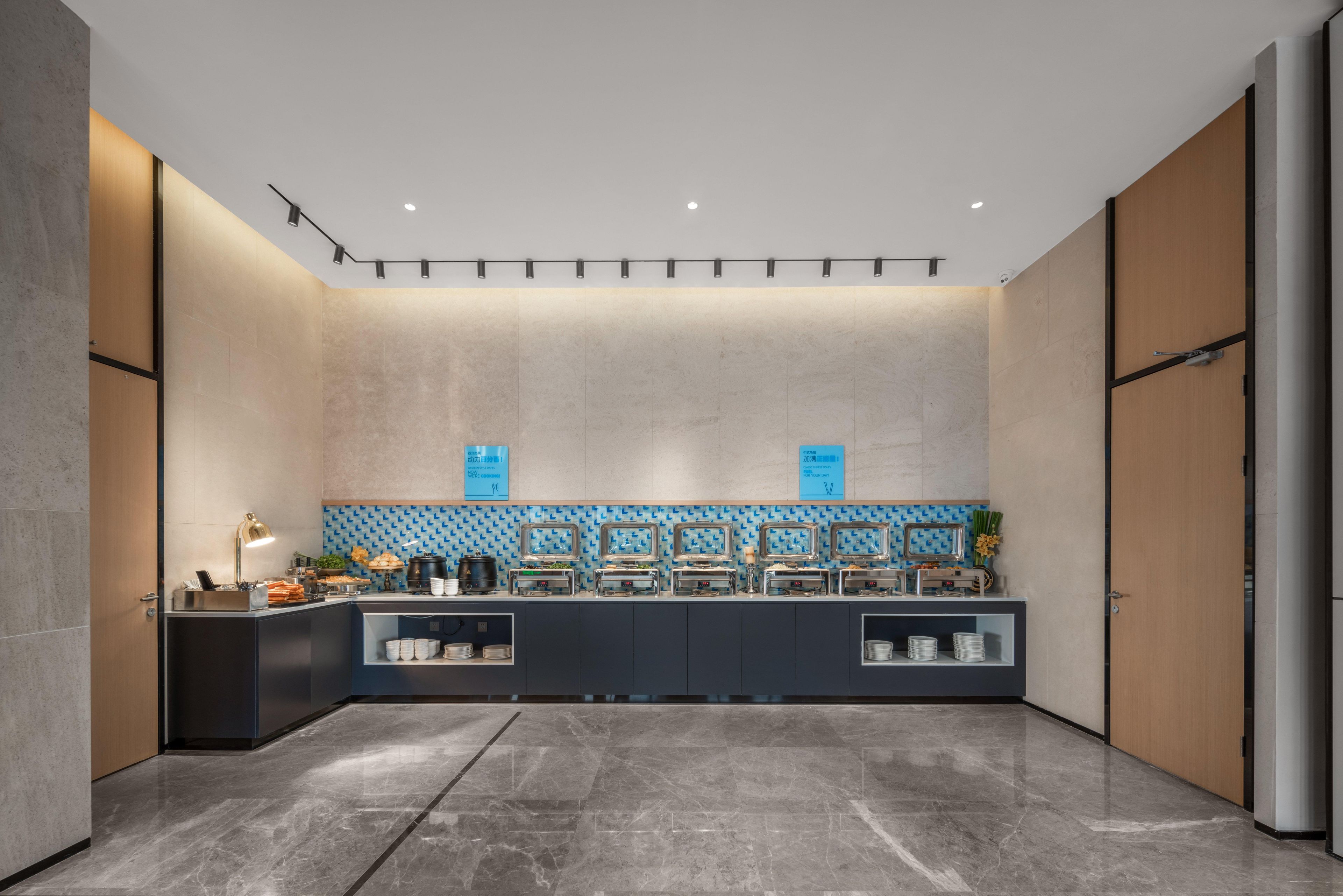 A modern hotel lobby with a reception desk, a buffet area, and a large mirror.