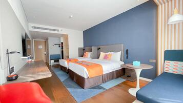 A modern hotel room with a large bed, a desk, a chair, and a small table.