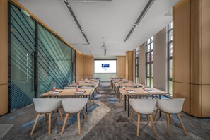 A conference room with a large screen, multiple tables, and chairs arranged for meetings. - Holiday Inn Express Yixing (Wuxi)