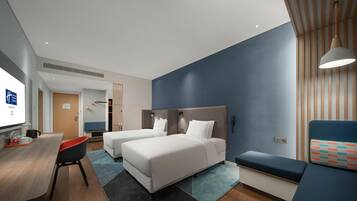 A hotel room with two beds, a desk, a chair, a sofa, and a TV.