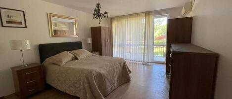 A bedroom with a bed, a nightstand, a dresser, a chandelier, and a sliding glass door leading to a balcony.