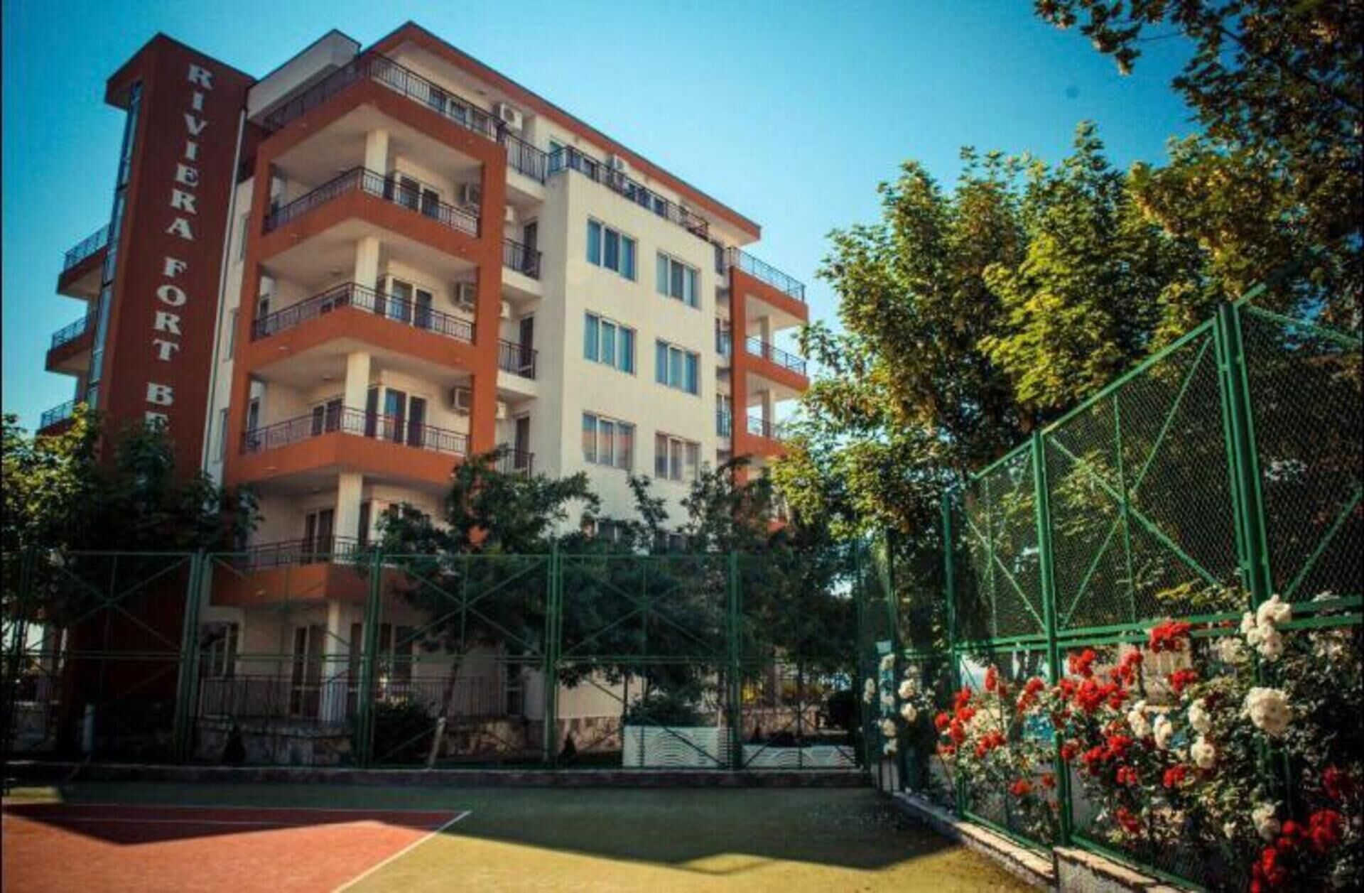 A multi-story hotel with balconies and a tennis court in the courtyard.