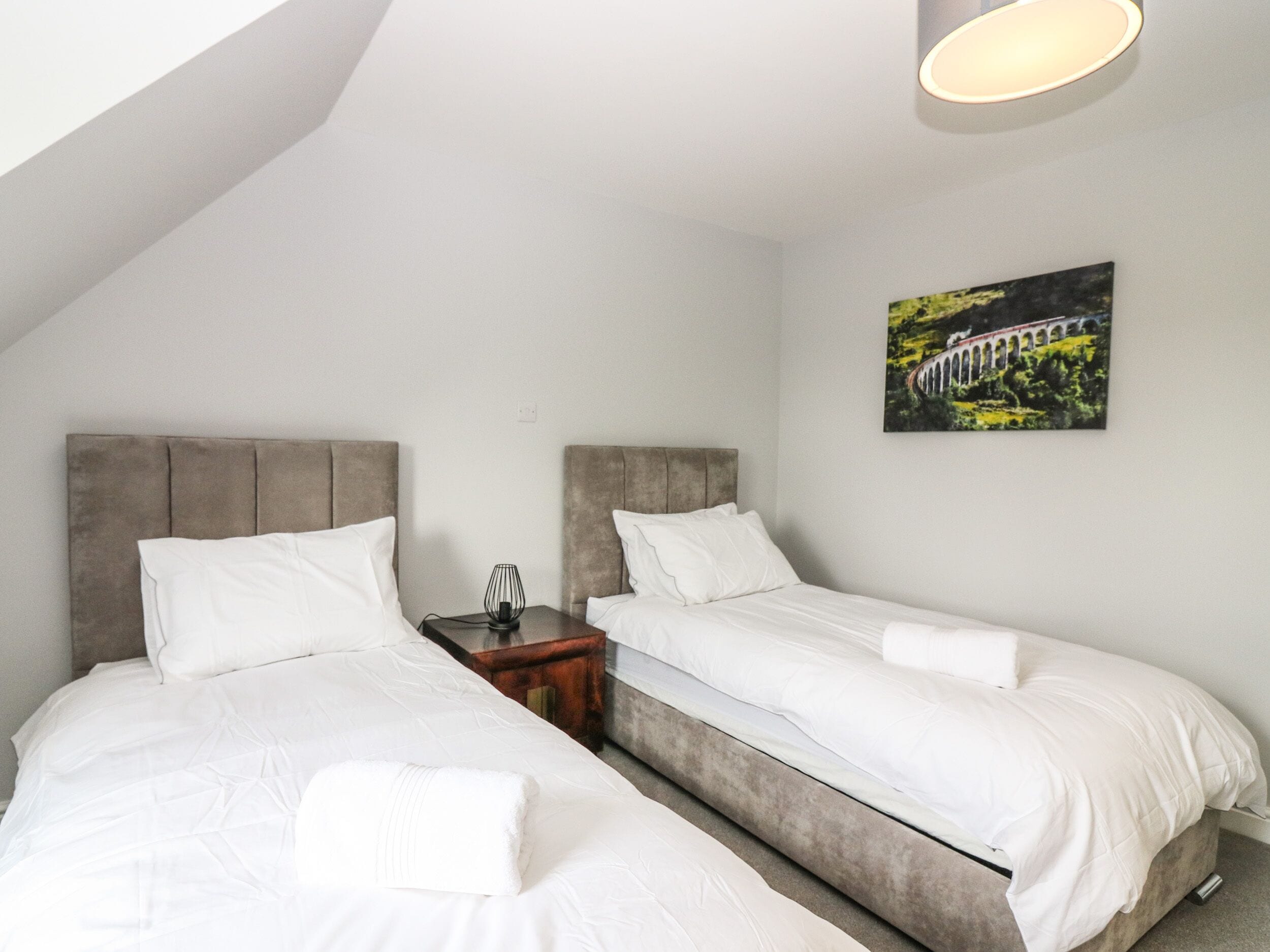A hotel room with two beds, a nightstand, a lamp, and a painting on the wall.