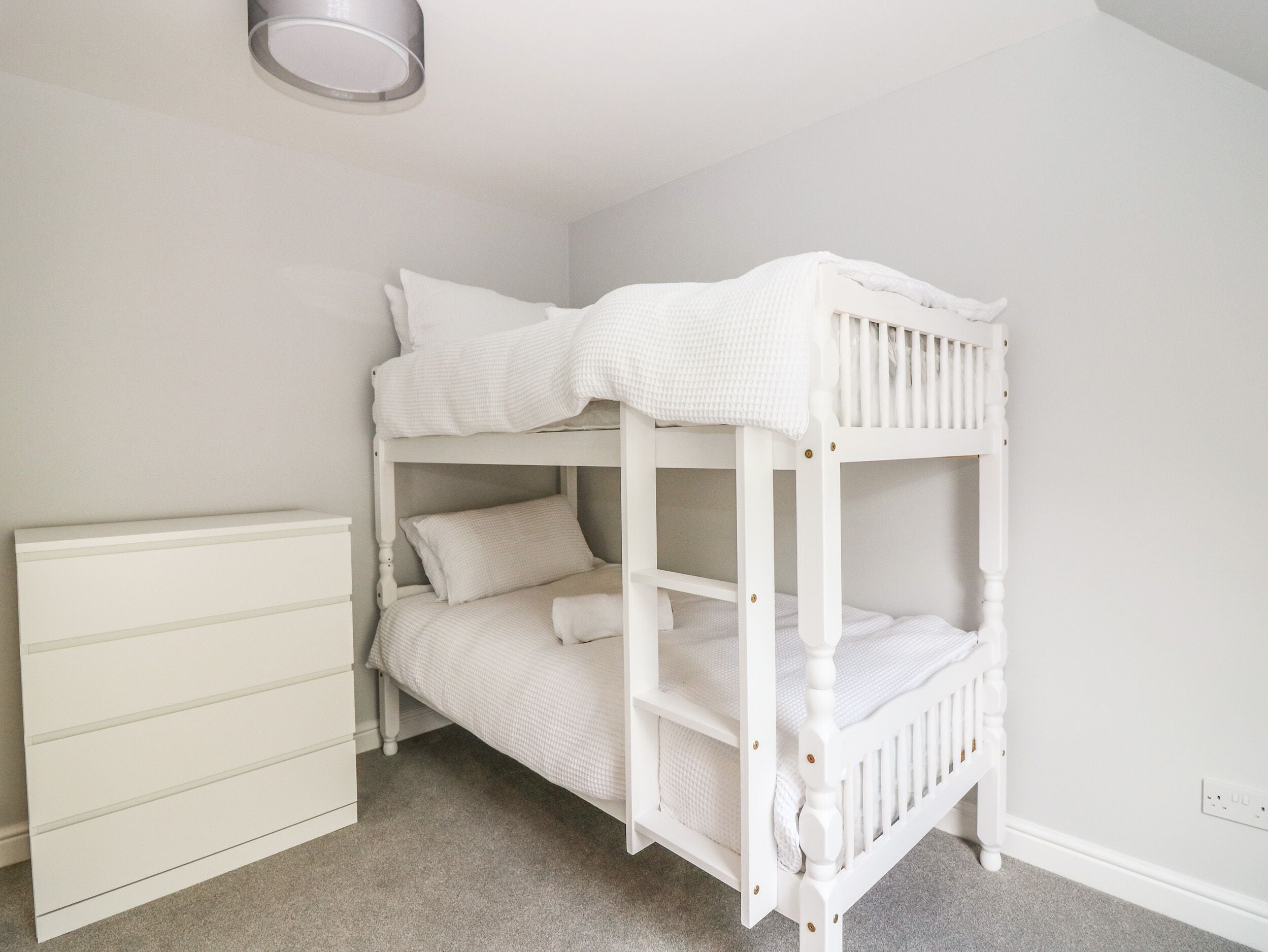 A bunk bed in a room with a white dresser and a light switch on the wall.