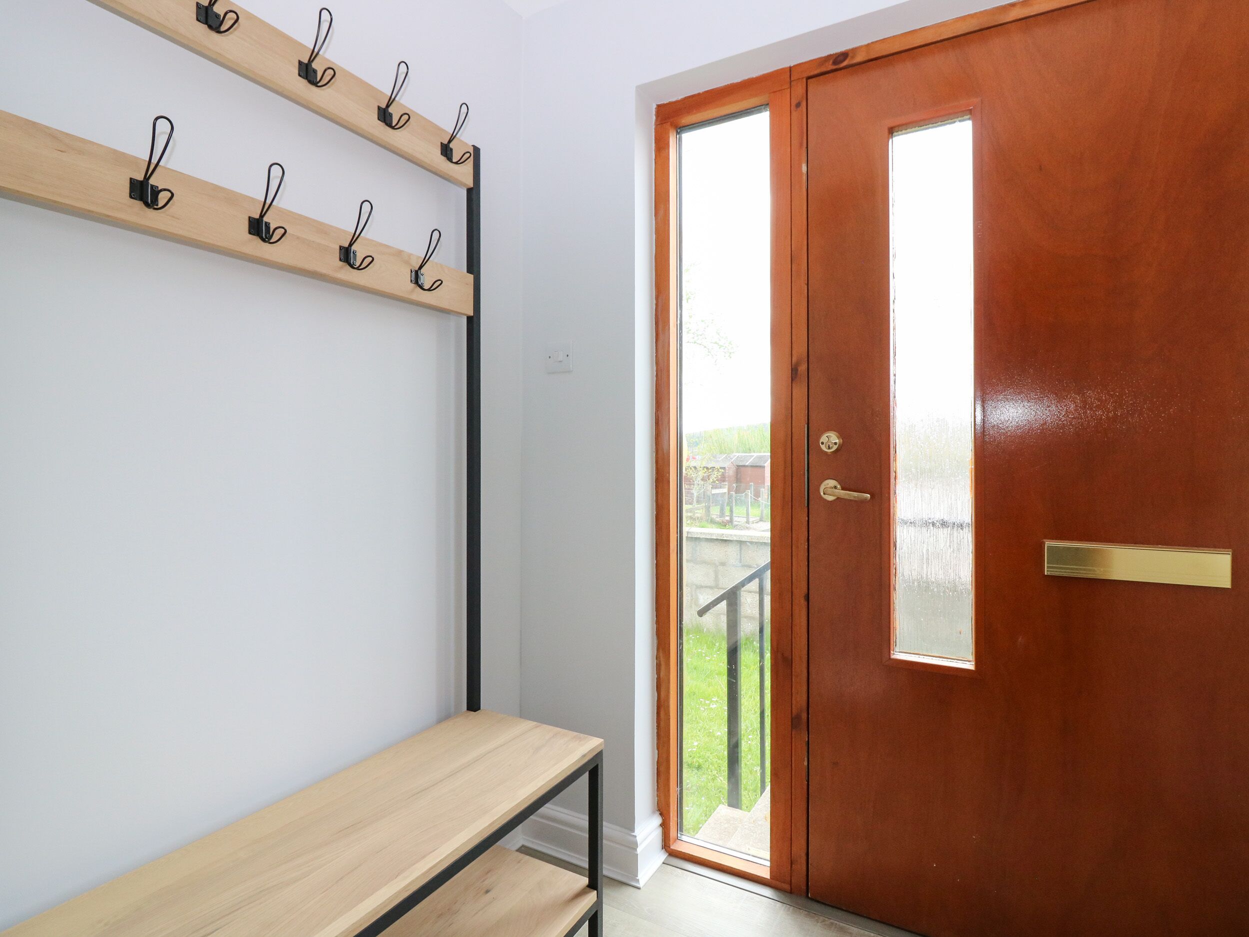 A room with a wooden bench, a coat rack with hooks, and a wooden door with a brass handle.