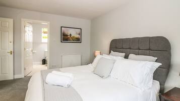 Un dormitorio con una cama grande, un radiador, un cuadro enmarcado en la pared y una puerta que da a otra habitación.