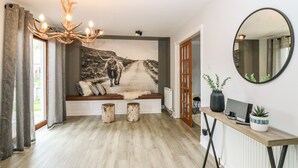 A room with a wooden floor, a bench with cushions, a chandelier, a large wall painting of a bull, a mirror, and a small table with a plant. - Tombeck (Ballindalloch)