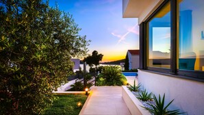 Ein modernes Haus mit gepflastertem Weg, einem gepflegten Garten und Blick auf den Sonnenuntergang.