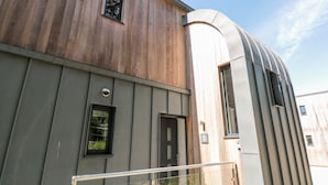 A modern building with a wooden upper section and a metallic lower section, featuring a curved metallic structure and a small window. - 3 The Hide (Plymouth)