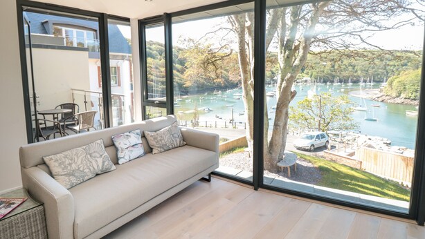 A modern living room with a large window overlooking a marina and hills. - 3 The Hide (Plymouth)