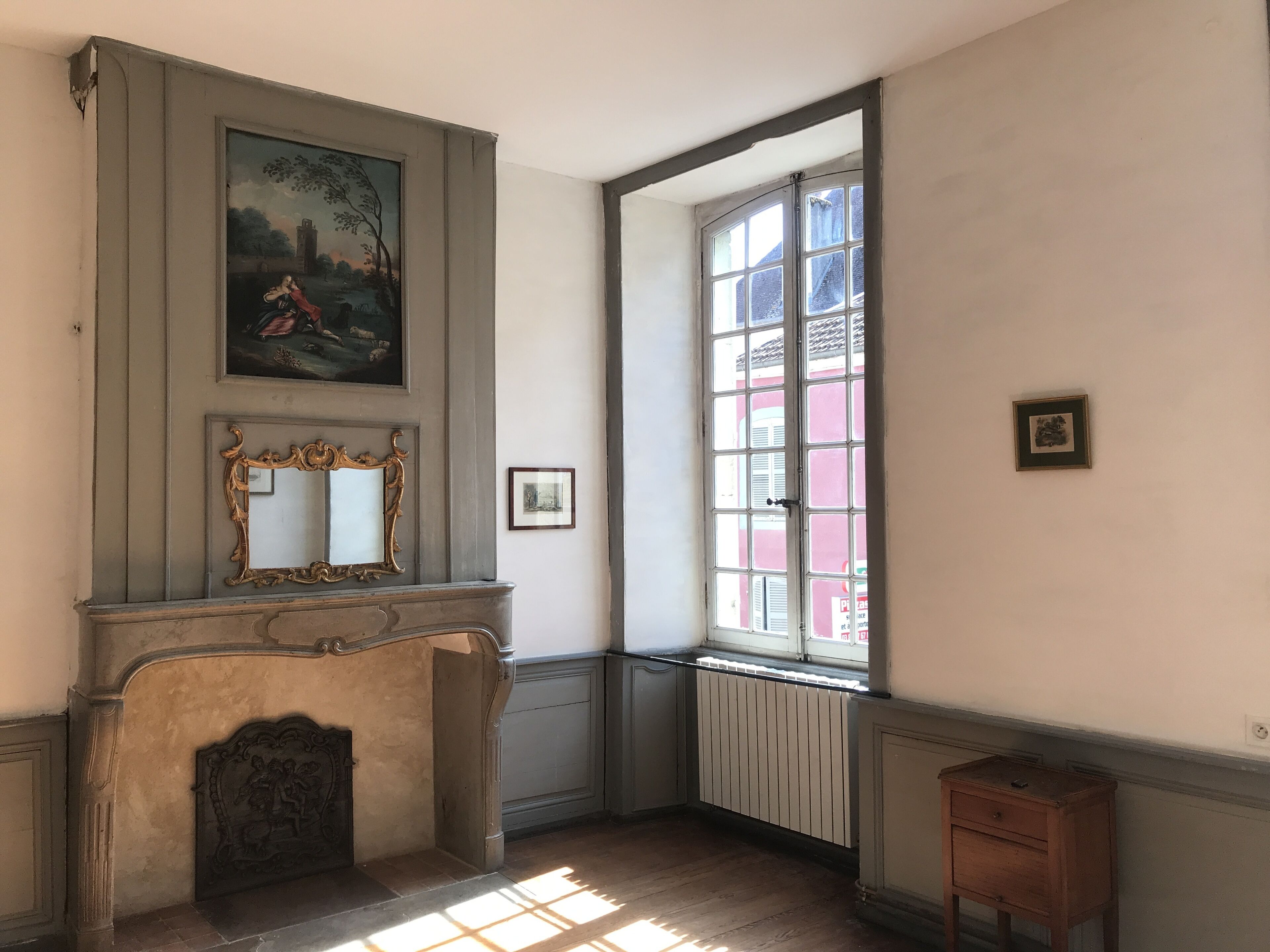 A room with a fireplace, a large window, and a painting on the wall.