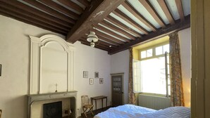 A bedroom with a bed, a fireplace, a window with curtains, and a wooden ceiling.