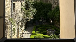 A narrow street with stone buildings, a clock tower, and a well-maintained garden.