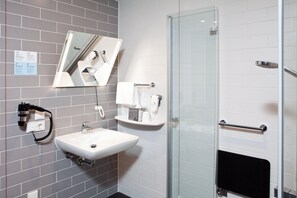 Un baño moderno con cabina de ducha de vidrio, un lavabo blanco con espejo y un perchero.