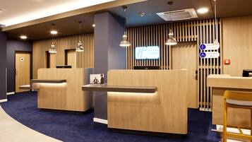 A modern hotel reception area with wooden reception desks, comfortable seating, and a digital screen displaying the hotel name.