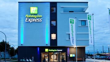 Edificio de Holiday Inn Express con un letrero llamativo, entrada de vidrio y un estacionamiento con bicicletas.