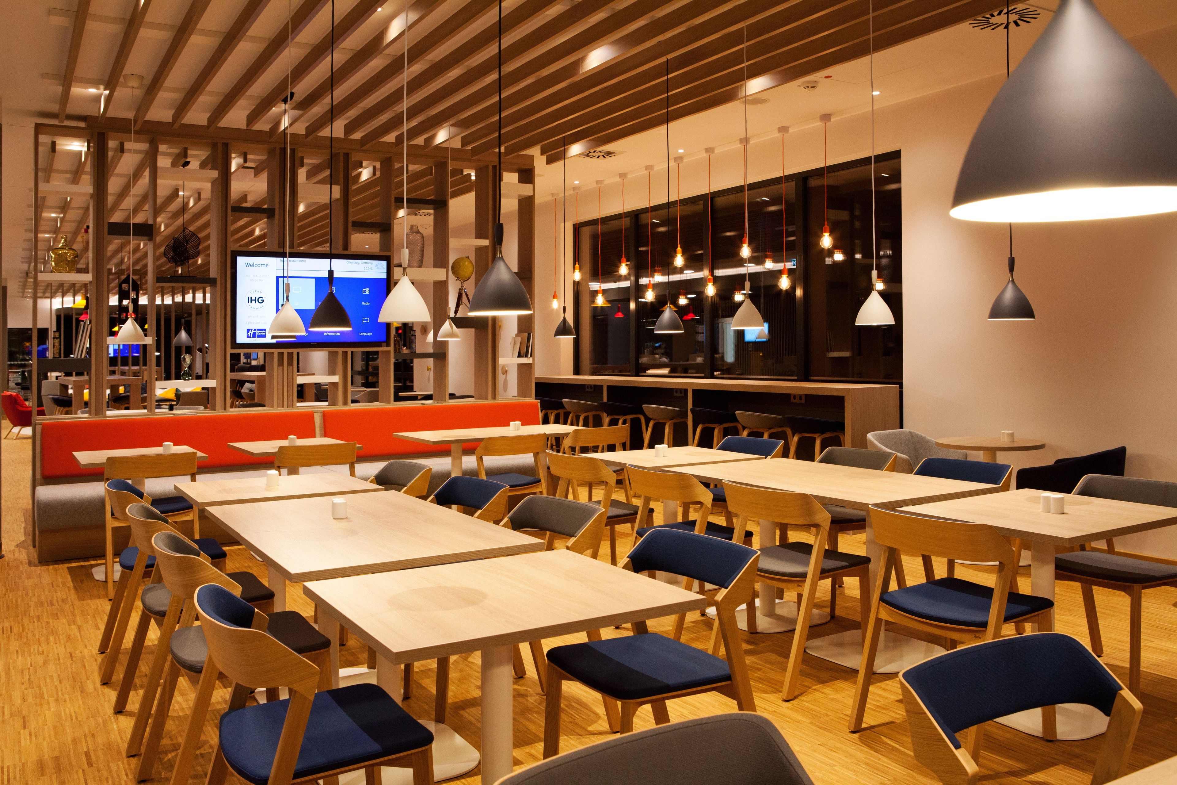 A modern dining area with wooden tables and chairs, a red booth seating area, and pendant lighting.