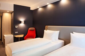 A hotel room with a large bed, a red chair, a small table, and a wall-mounted light. - Holiday Inn Express Offenburg (Offenburg)
