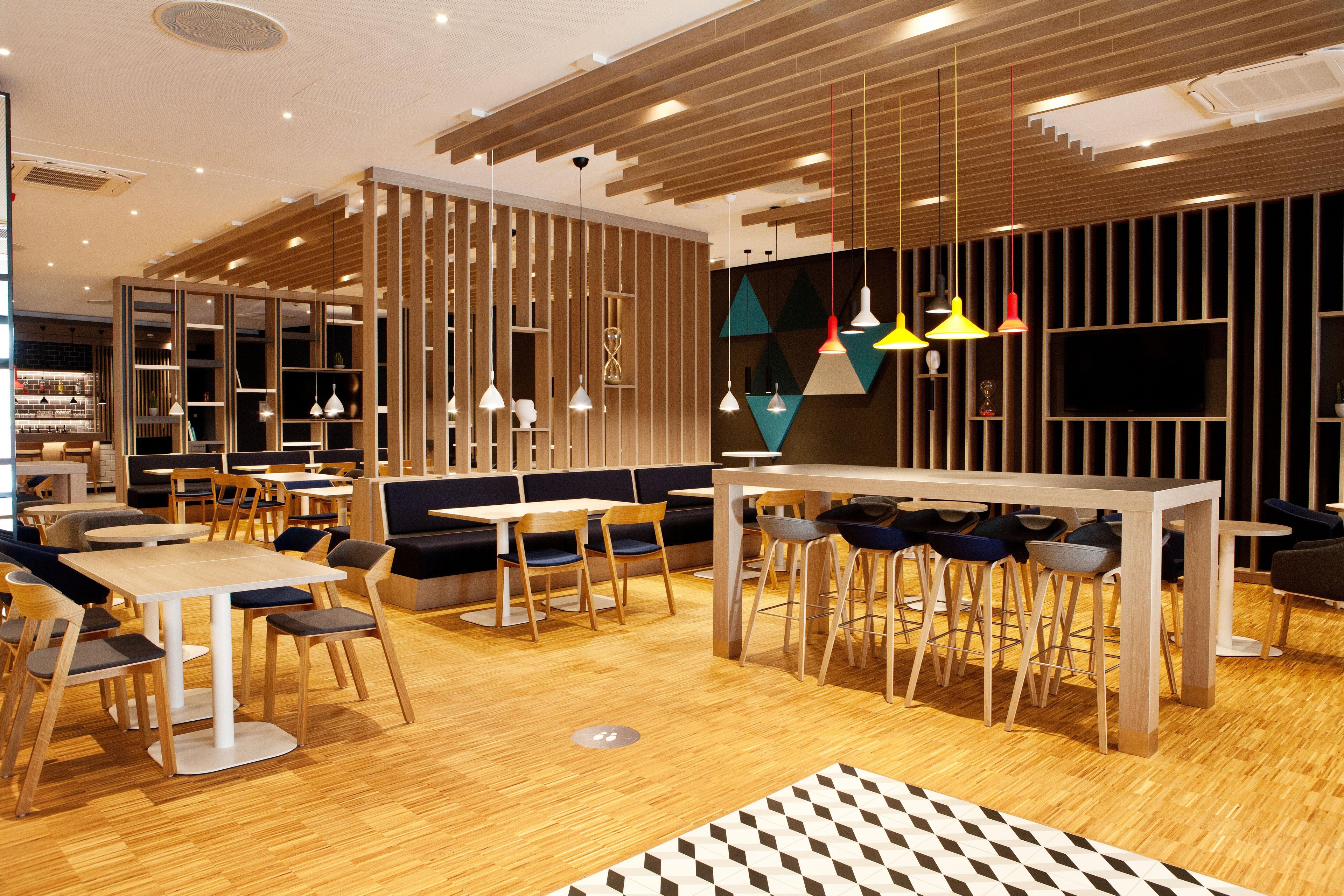 A modern restaurant with wooden flooring, multiple seating areas including booths and tables, and pendant lighting.