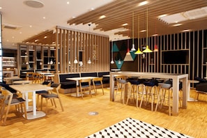 Un restaurant moderne doté d’un plancher en bois, de plusieurs espaces de restauration, notamment des banquettes et des tables, et d’un éclairage suspendu.