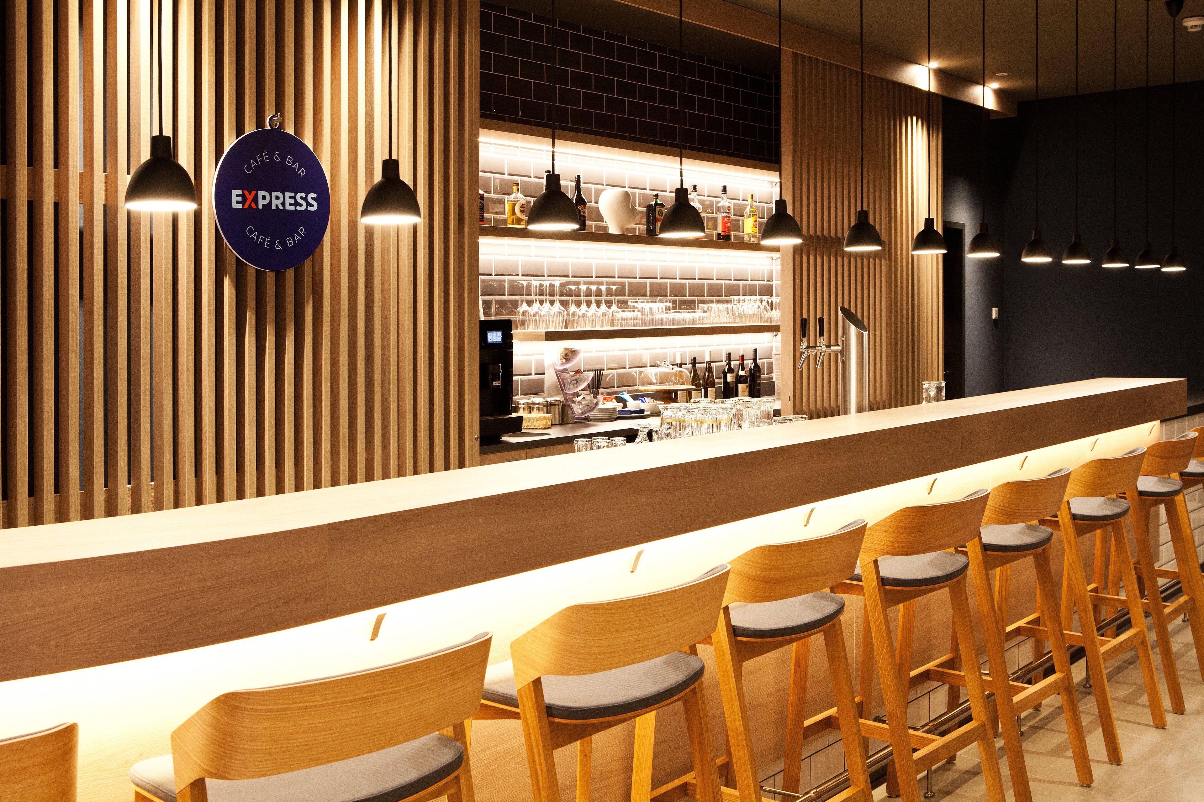 A modern bar area with wooden slats, a long counter, and multiple bar stools.