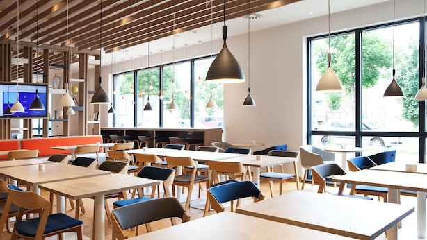 A modern dining area with tables and chairs, large windows, and pendant lighting.