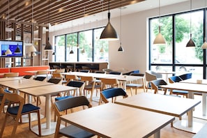 Un comedor moderno con mesas y sillas, ventanas amplias e iluminación colgante.