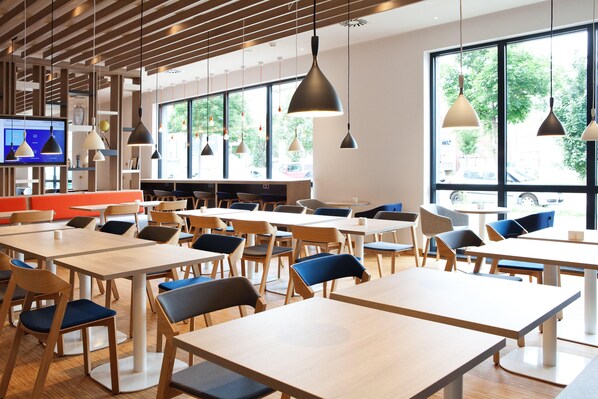 Un comedor moderno con mesas y sillas, ventanas amplias e iluminación colgante.