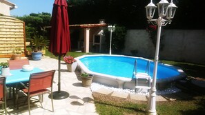 Una piscina con borde de baldosas, rodeada de plantas en macetas y mobiliario de exterior.