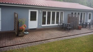 Een gebouw met een pannendak, een overdekte patio met een tafel en stoelen, en een deur met een raam.