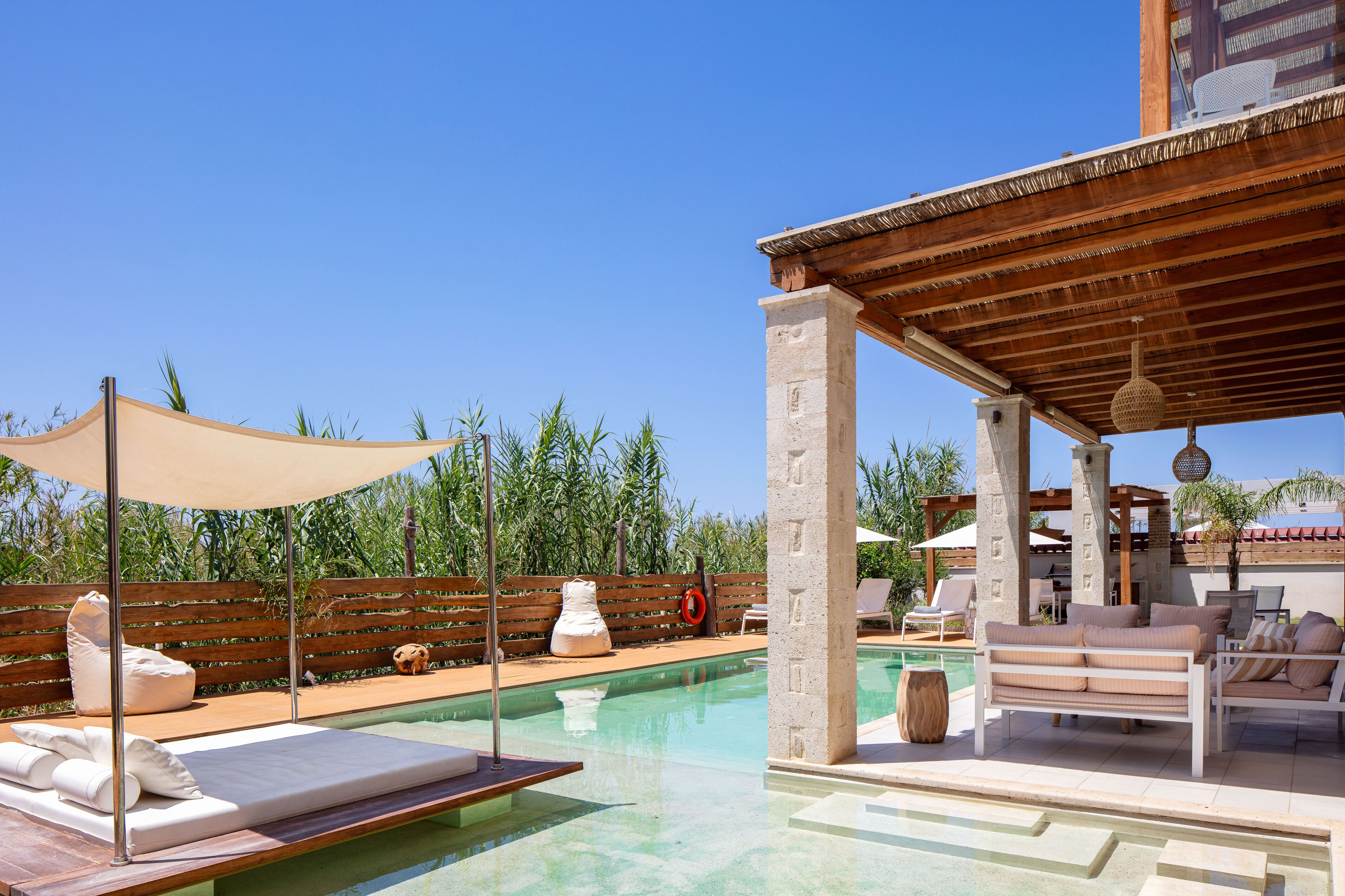 A pool area with lounge chairs, a wooden pergola, and a clear blue sky.