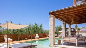 Een zwembadgedeelte met ligbedden, een houten pergola en een helderblauwe lucht.