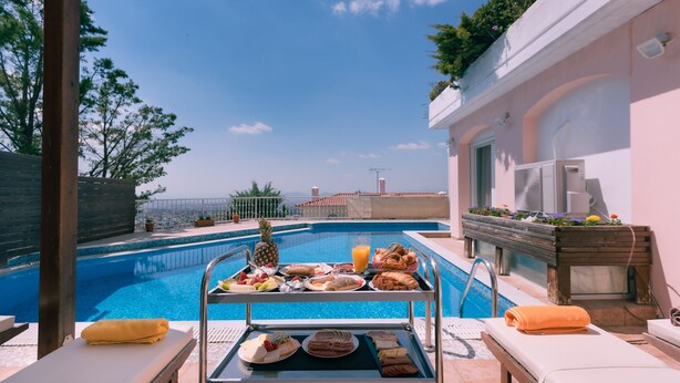 A poolside breakfast setup with a variety of foods and a pineapple, overlooking a swimming pool. - Villa Politia   Luxury Villa with a Spectacular City View (Athens)