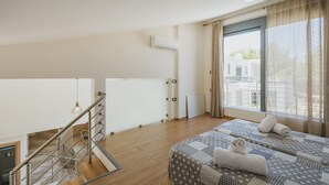 A hotel room with a wooden floor, a bed with a patterned bedspread, a window with curtains, and a staircase with a metal railing. - Park-View Pool Villa steps to the Beach (Chania)