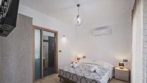 A modern hotel room with a bed, bedside tables, a ceiling light, and an air conditioning unit. - Park-View Pool Villa steps to the Beach (Chania)