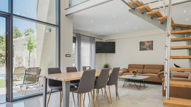 A spacious living area with a dining table, chairs, a sofa, and a staircase. - Park-View Pool Villa steps to the Beach (Chania)