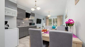 A modern kitchen with grey cabinets, a dining table with two chairs, and a vase of flowers. - Bright apartment with balcony | Right on the beach in Miedzywodzie (Międzywodzie)