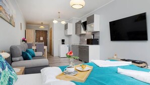 A modern hotel room with a bed, a sofa, a dining table with a tray of breakfast, a coffee cup, and a TV. - Bright apartment with balcony | Right on the beach in Miedzywodzie (Międzywodzie)